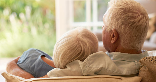 Older Couple Cuddling On Sofa Backs To Camera